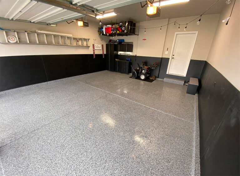 The image shows a tidy garage interior with a speckled epoxy floor, storage shelves, a workbench, and a snowblower in the corner.