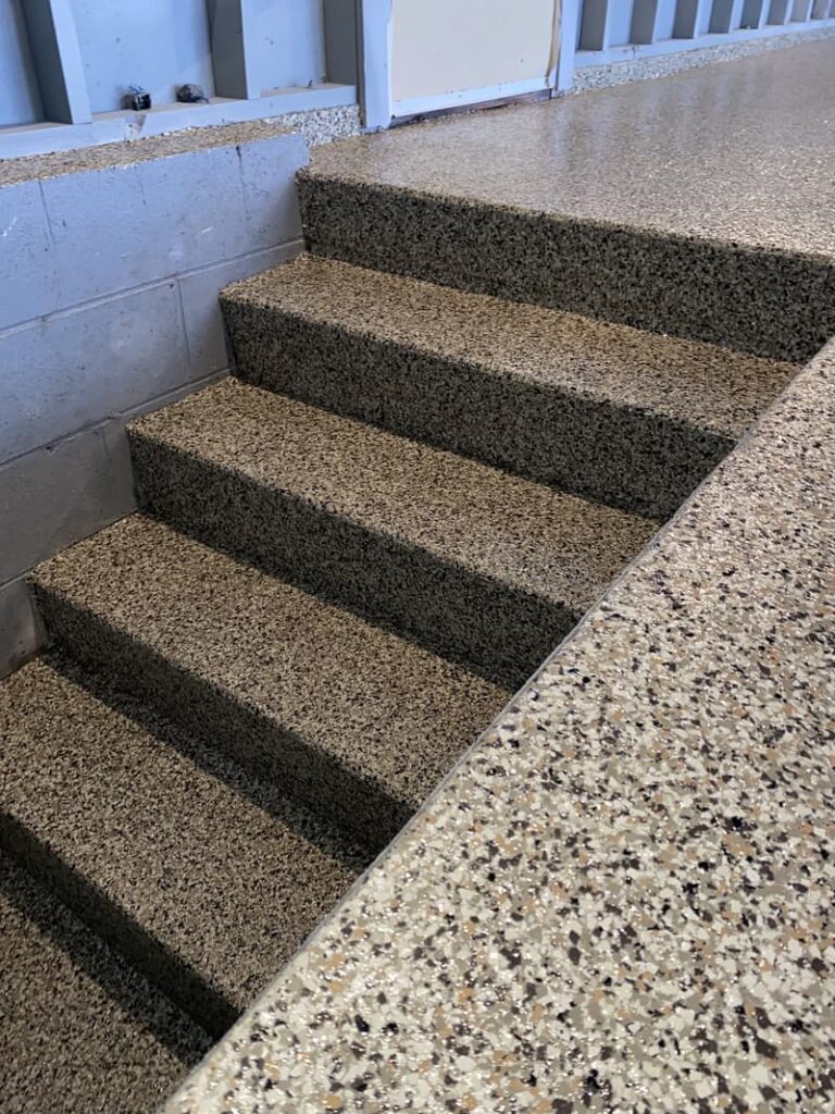 A flight of terrazzo stairs inside a building with speckled patterns, leading up to a landing with railing visible in the background.