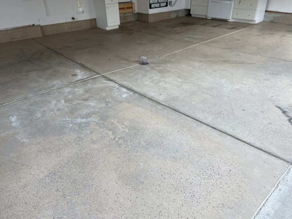 This image depicts a concrete floor in a garage or industrial space with a small object in the center, and white cabinetry against the back wall.